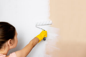 Girl Child Yellow Gloves Paints Wall With Roller With White Paint