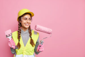 Positive Busy Female Builder Involved Renovation Repair Building Holds Roller Paint Brush Follows Strict Safety Regulations Wears Protective Equipment Has Leadership Skills Copy Space