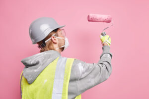 Sideways Shot Busy Handyman Dressed Safety Uniform Holds Paint Roller Wears Protective Mask Works Hard Isolated Pink Wall Repair Renovation Concept Maintenance Worker