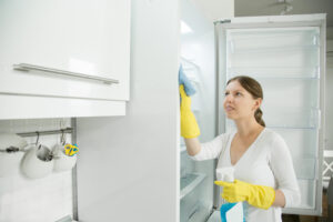 Young Woman Wearing Rubber Gloves Cleaning Fridge