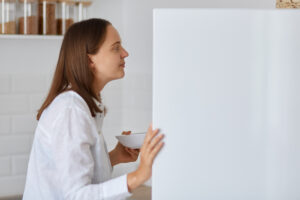 Side View Portrait Dark Haired Woman Looking Something Fridge Home Standing With Plate Hands Wearing White Shirt Feels Hungry Finds Food 1