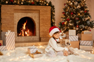 Good Looking Female Child Playing With Her Pekingese Dog Little Girl Wearing White Sweater Santa Claus Hat Posing Festive Room With Fireplace Xmas Tree