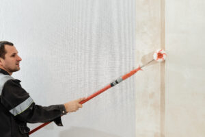 Man Worker Applies Glue With Paint Roller Walls Before Wallpapering Primer Walls Selective Focus Apartment Renovation Restoration Idea Indoors